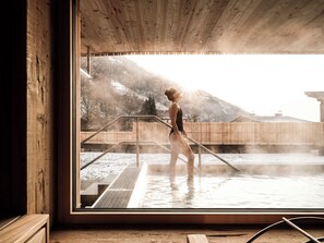 A person in a wooden cabin with a view of a snowy outdoor area and mountains. - Naturhotel Outside (Matrei in Osttirol)