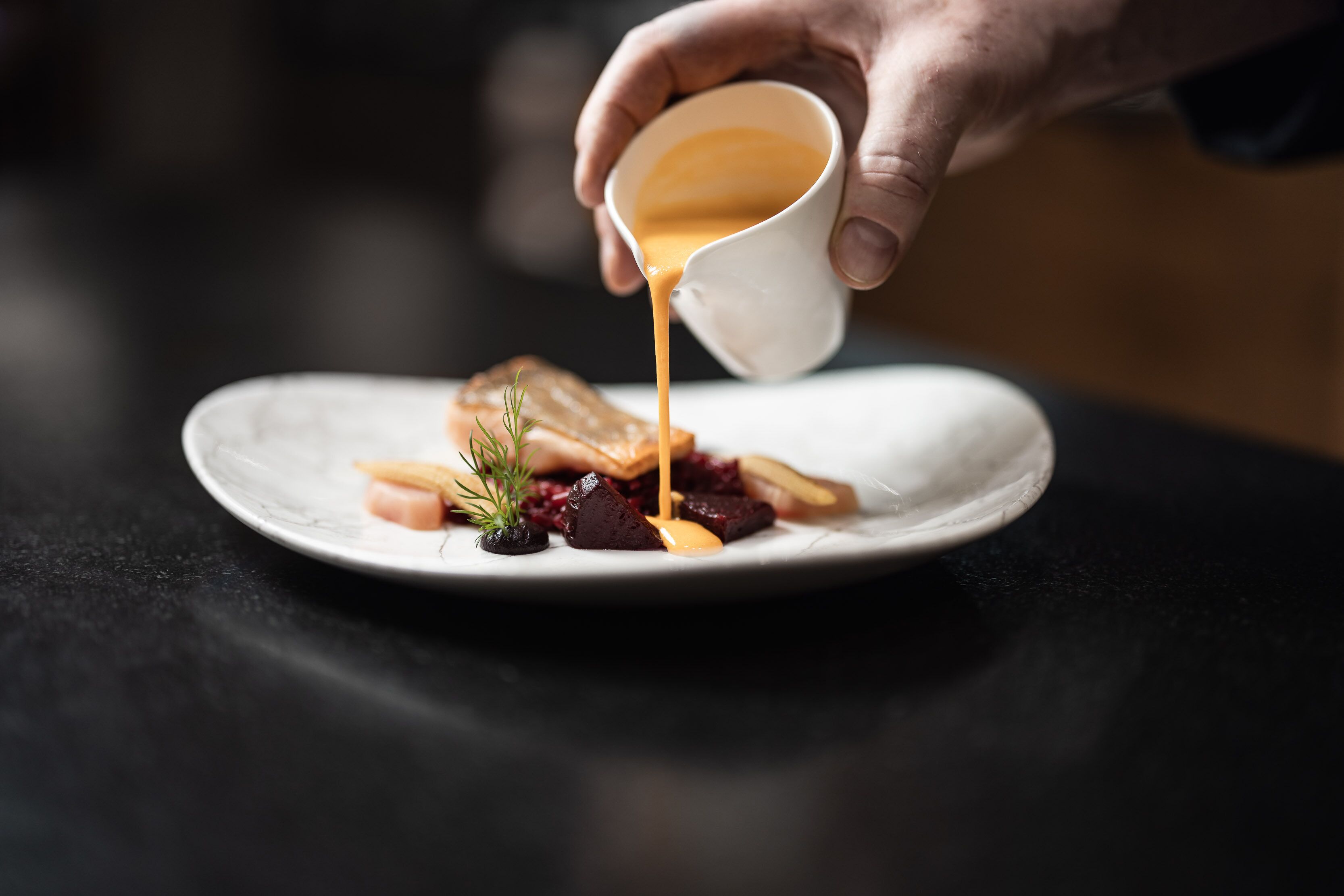 A hand pouring sauce onto a plate with food items.