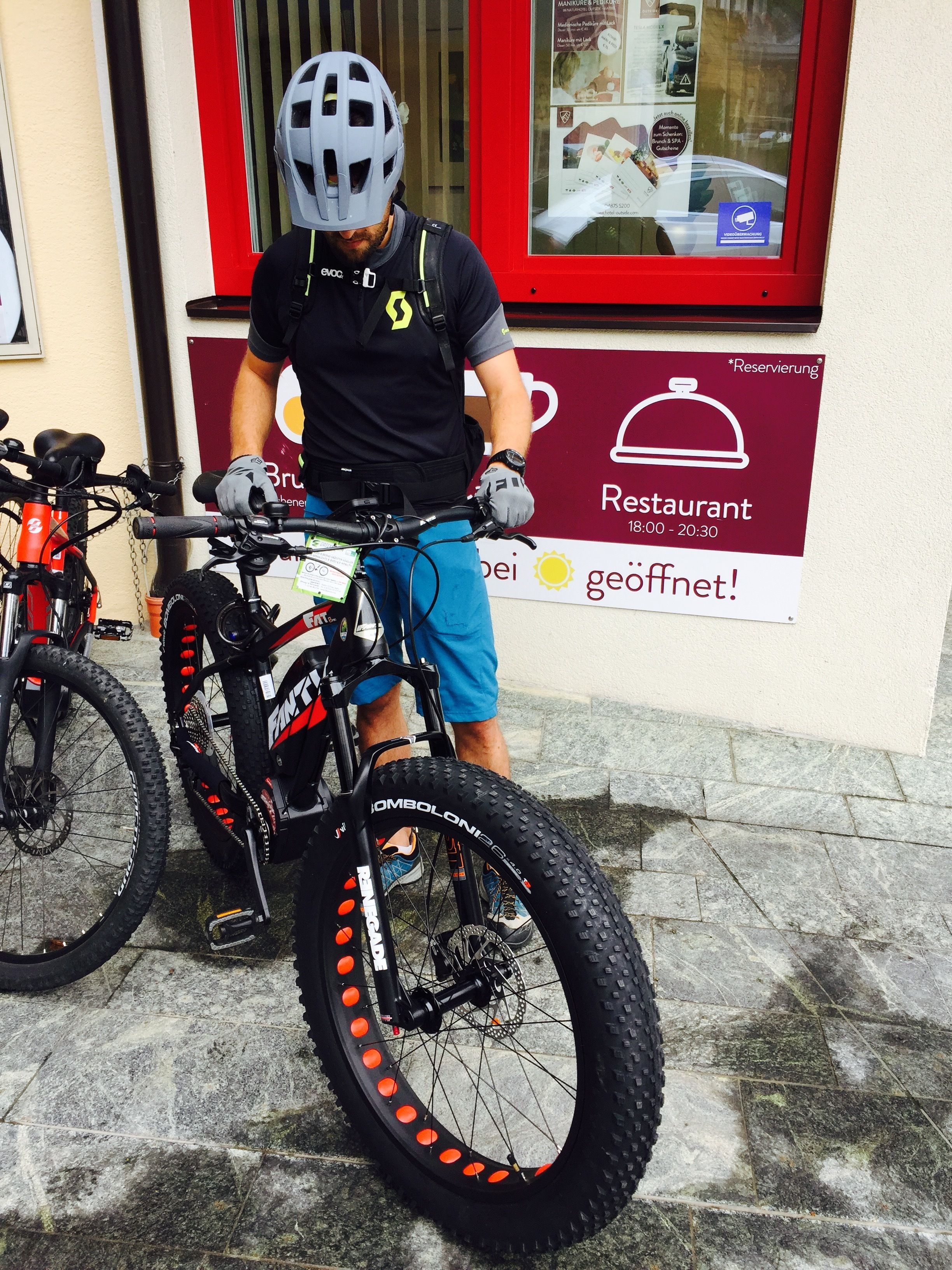 A person standing next to a mountain bike in front of a restaurant sign.