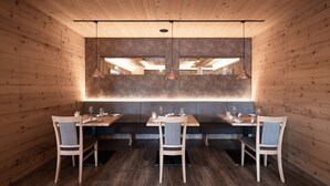 A wooden interior with a long table and chairs, a bench, and pendant lighting. - Naturhotel Outside (Matrei in Osttirol)