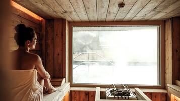 A wooden cabin with a sauna, a window with a view of a wooden deck, and a stone bench.