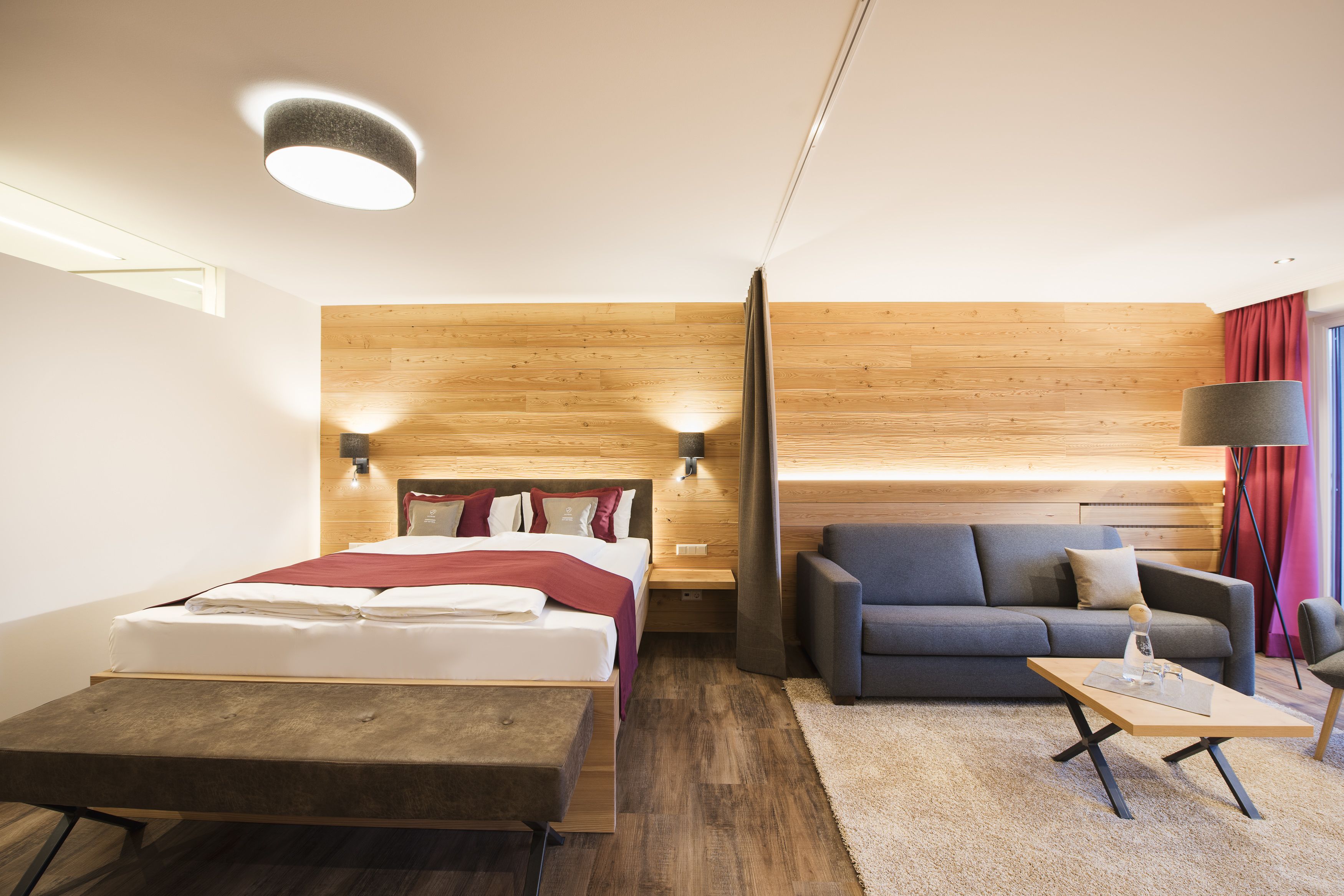 Una habitación de hotel moderna con un muro decorativo de madera, una cama, un sofá, una mesita de café y una lámpara.