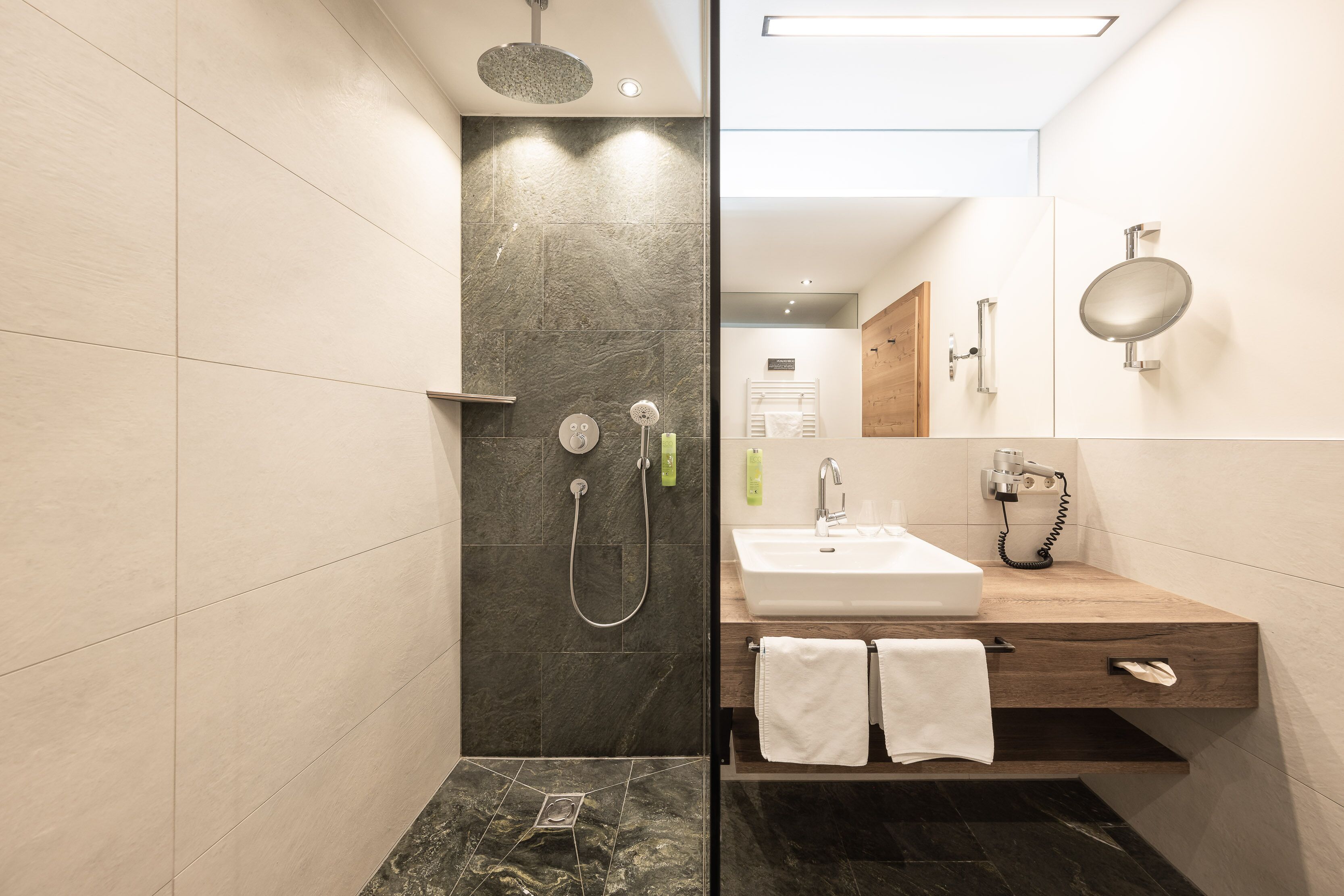 A modern bathroom with a glass shower enclosure, a wooden vanity with a white sink, and a large mirror.