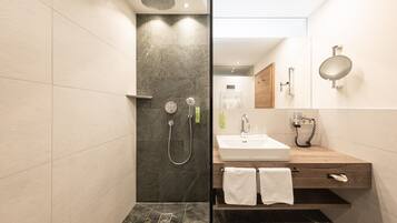 A modern bathroom with a glass shower enclosure, a wooden vanity with a white sink, and a large mirror.
