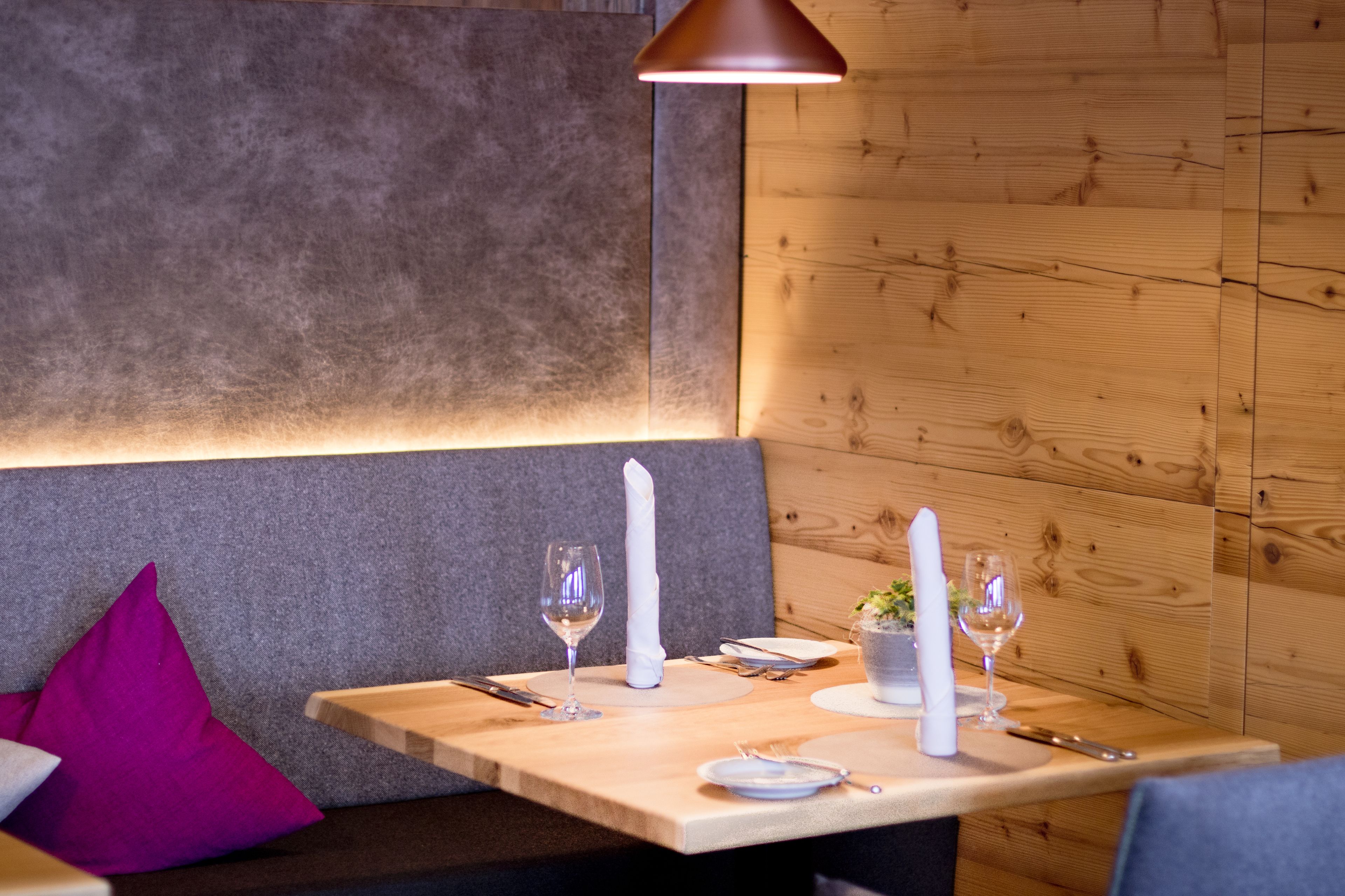 A wooden dining table with a candle, wine glasses, and cutlery.