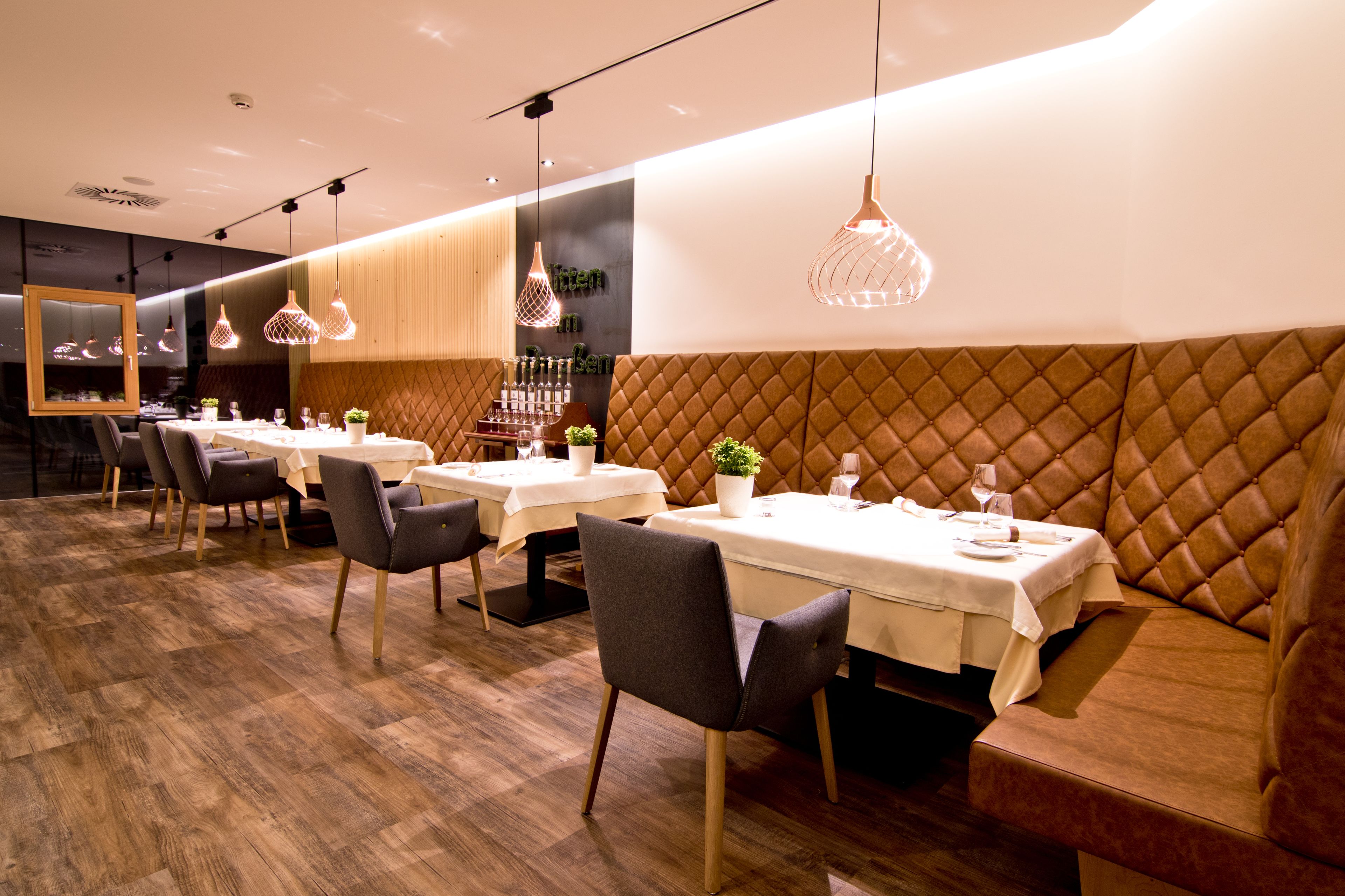 A modern dining area with wooden flooring, cushioned seating, and pendant lighting.