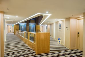 A hotel corridor with a striped carpet, a wooden reception desk, and a staircase leading to elevators. - Metropark Hotel Macau (Macau)
