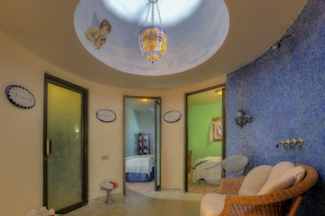 A room with a ceiling mural, a hanging lamp, a wicker chair, and a bed with a blue bedspread.