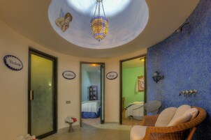 Una habitación con un mural en el techo, una lámpara colgante, una silla de mimbre y una cama con colcha azul.