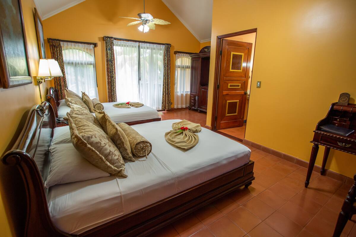 A hotel room with two beds, a wooden headboard, a ceiling fan, and a wooden wardrobe.