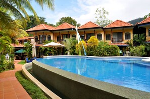 A swimming pool with a tiled deck, surrounded by a building with multiple balconies and a tropical garden. - Hotel Cuna Del Angel (Bahía Ballena)