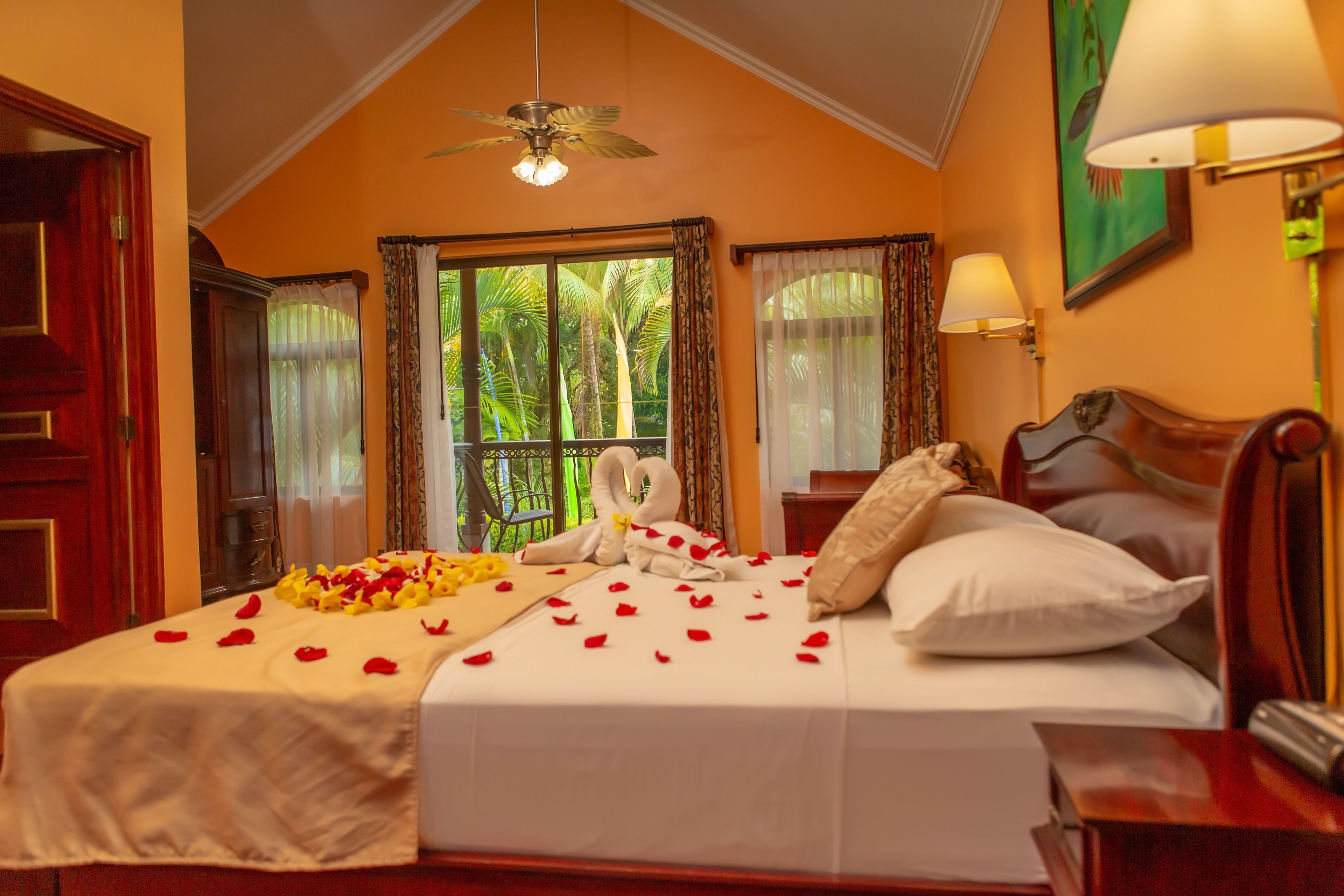 A hotel room with a bed, a nightstand, a lamp, a ceiling fan, and a window with curtains.