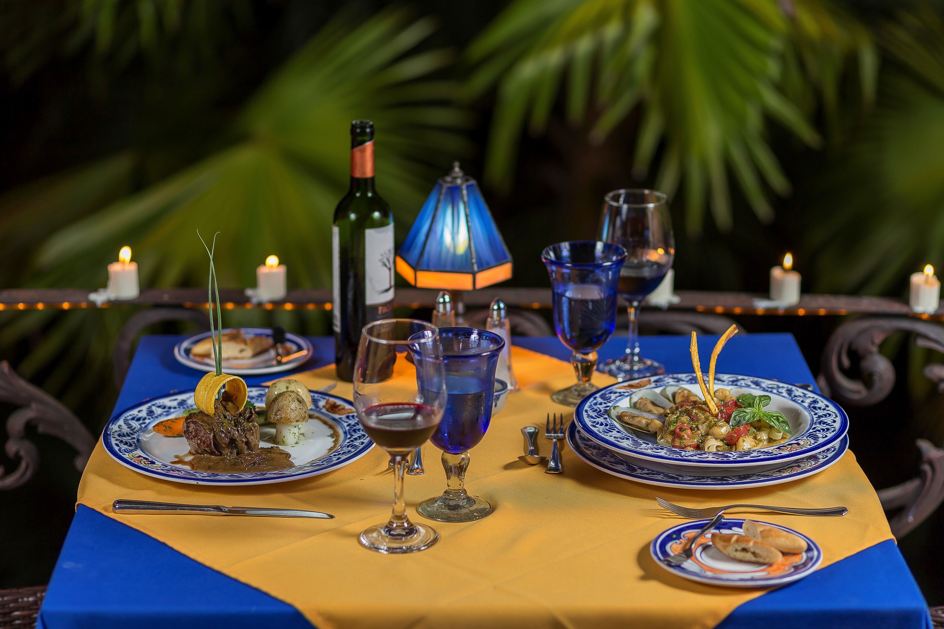 A table set for a meal with plates, glasses, and a bottle of wine, surrounded by candles and greenery.