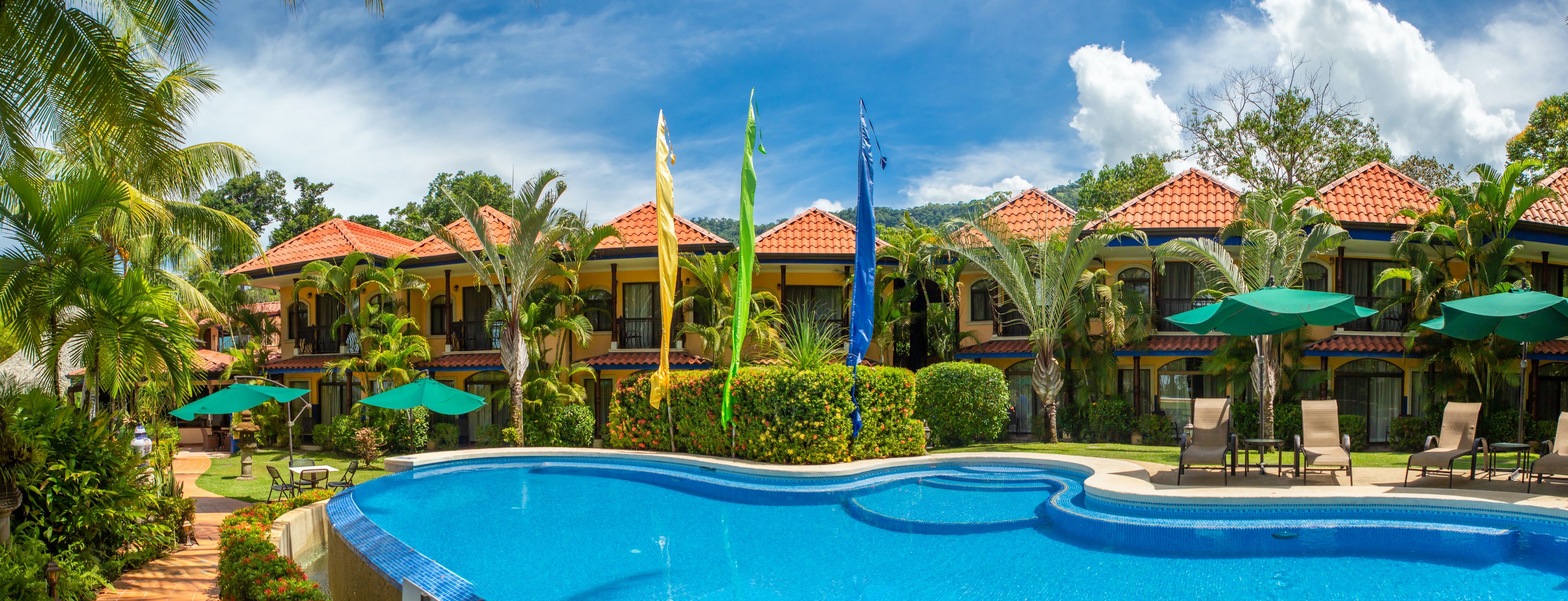 A resort with a swimming pool, palm trees, and a clear blue sky.