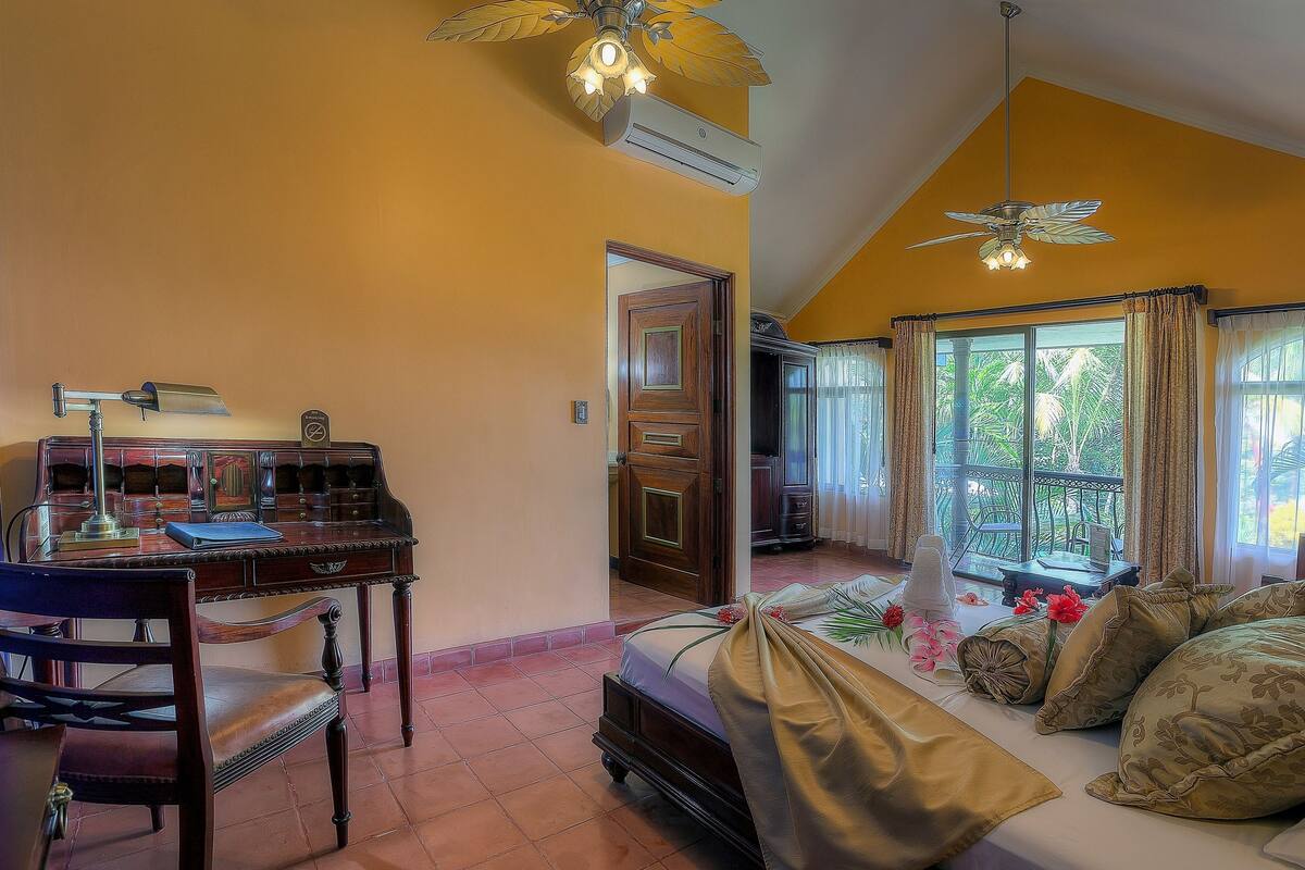 A room with a bed, a desk with a lamp, and a ceiling fan.