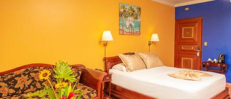 A hotel room with a bed, a sofa, a painting, and a nightstand.