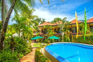 A resort with a swimming pool, palm trees, and a building with a red-tiled roof. - Hotel Cuna Del Angel (Bahía Ballena)