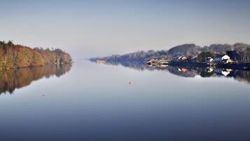A calm lake with a reflection of houses and trees, surrounded by a forested area.
