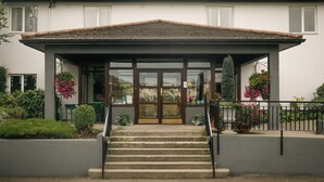 A building with a covered entrance, steps leading up to it, and potted plants with flowers. - Downhill Inn (Ballina)