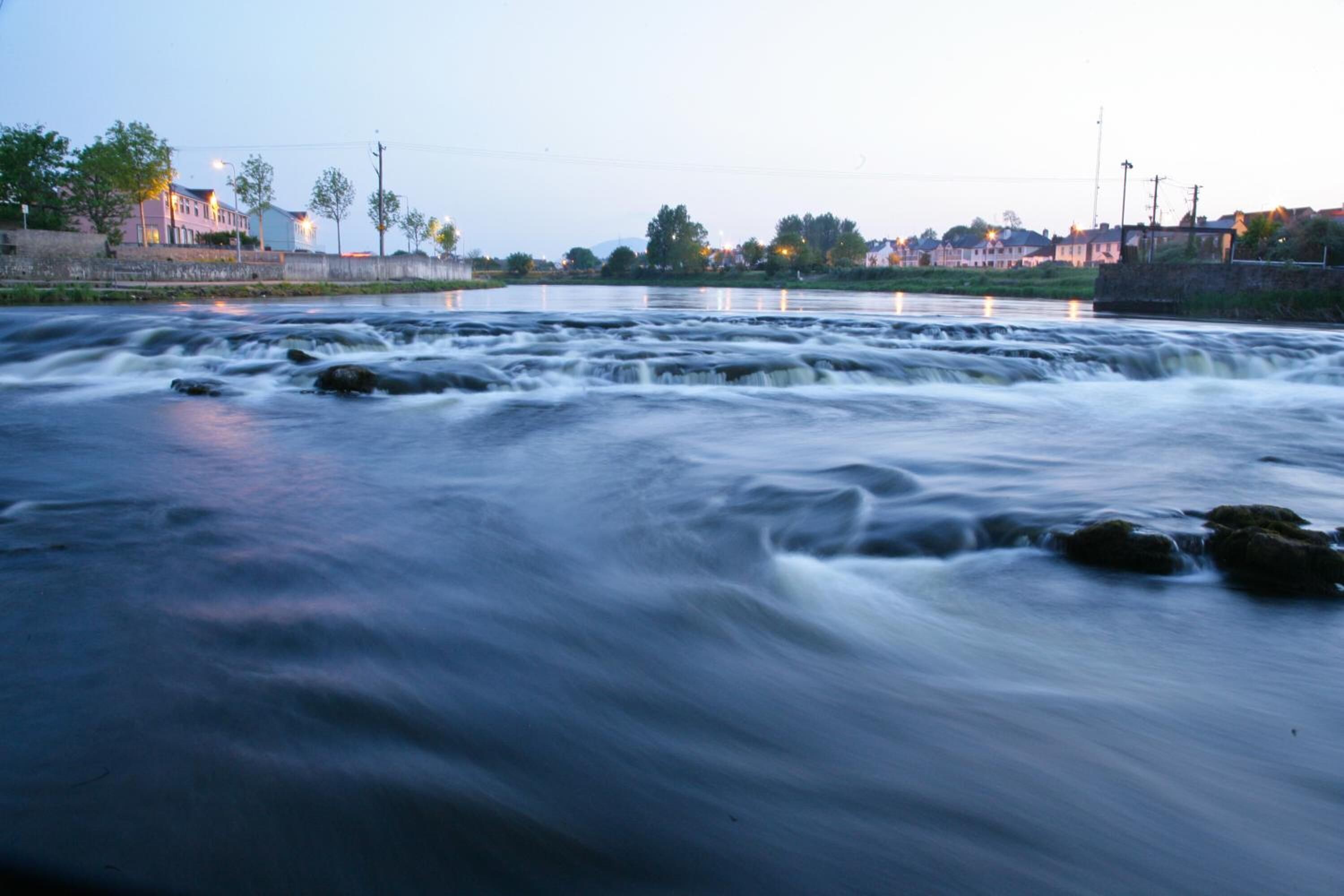 A river with a smooth flow, surrounded by buildings and trees.