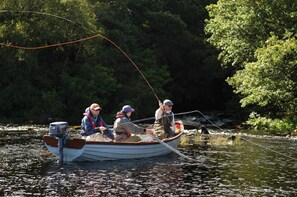 A small boat on a river with three people fishing.