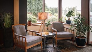 A room with two wooden chairs, a small table, and a lamp. There are potted plants and a view of greenery outside the window. - Downhill Inn (Ballina)