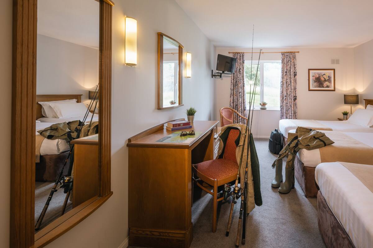 A hotel room with two beds, a desk with a chair, a television, and a large mirror.