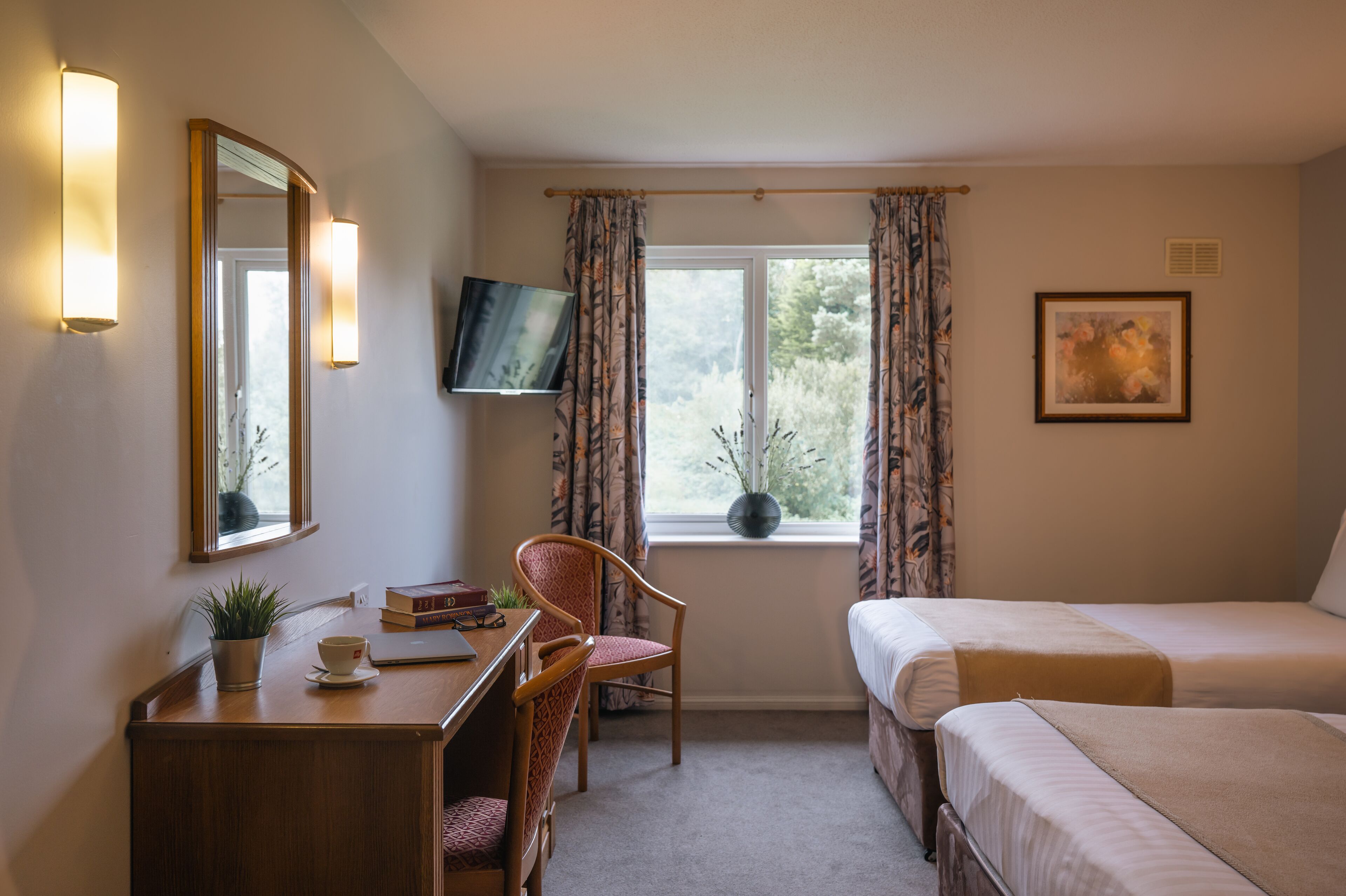 Habitación de hotel con escritorio, silla, dos camas, televisor y ventana con cortinas.