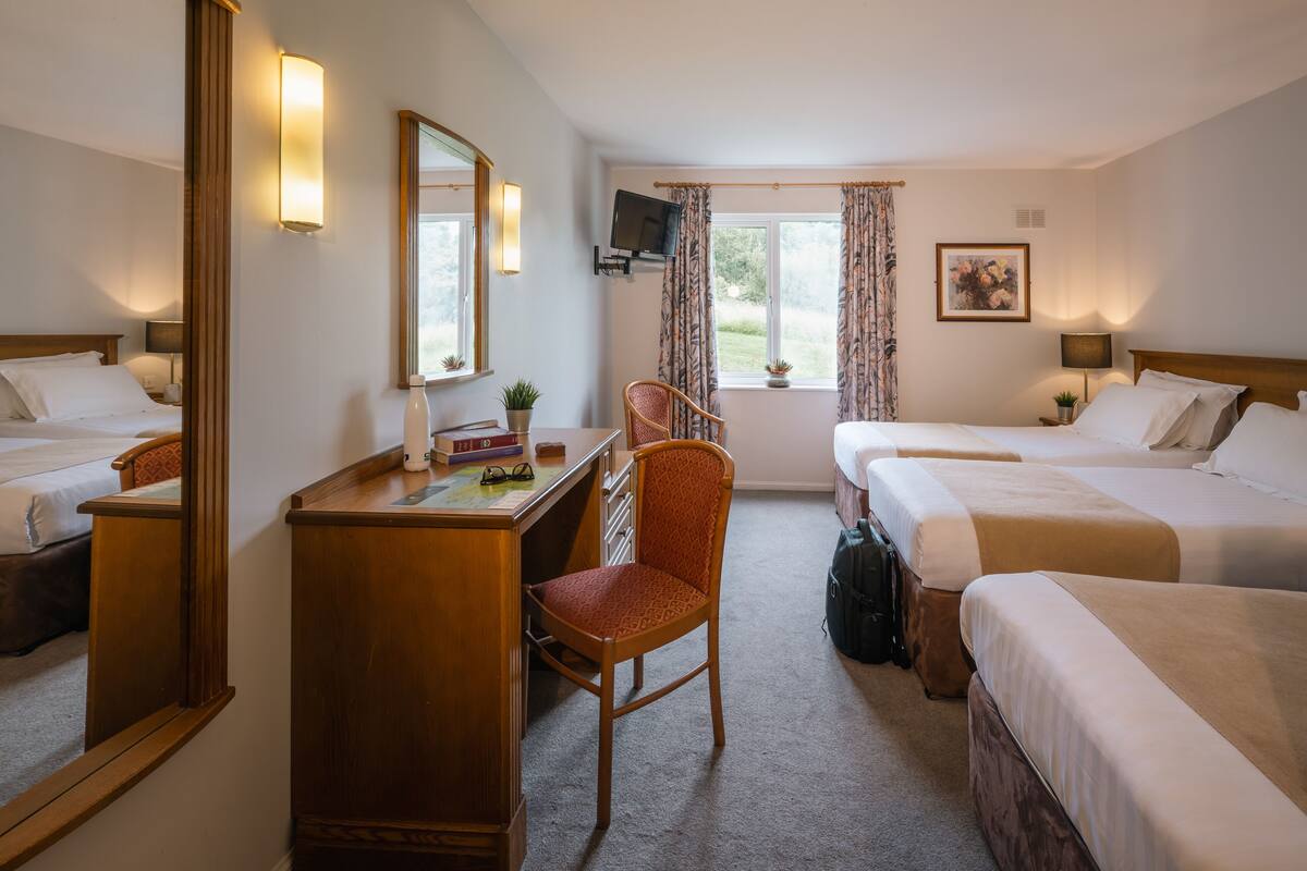 A hotel room with two beds, a desk, a chair, a TV, and a window with curtains.