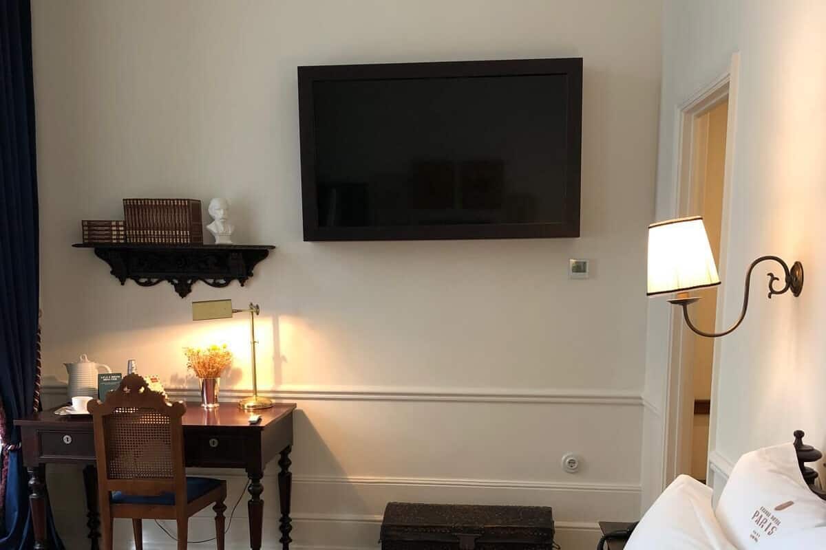 Een hotelkamer met een bed, een bureau met stoel, een aan de muur bevestigde televisie en een nachtkastje met lamp.