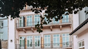 Un edificio de varios pisos con balcones, fachada de piedra y un patio con césped.