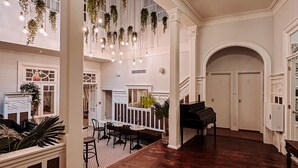 Un vestíbulo espacioso con un piano de cola, plantas colgantes y un alto techo con candelabro.