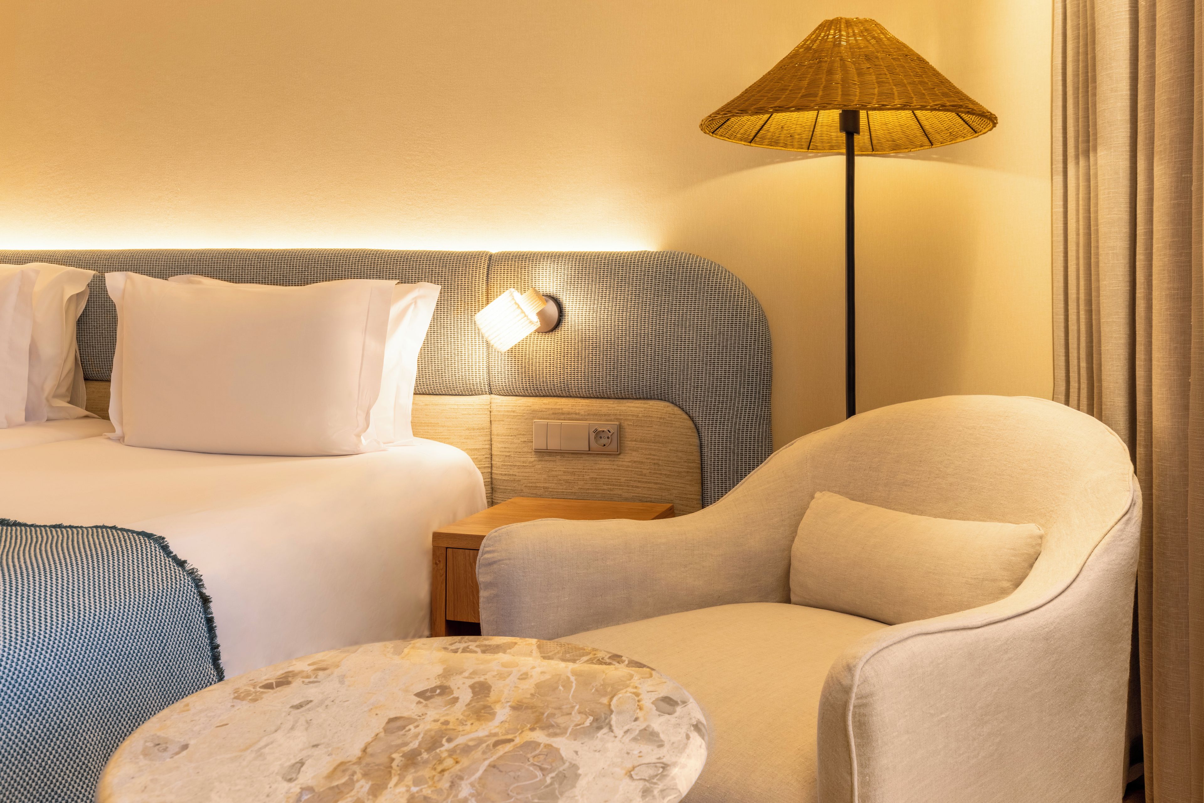 A hotel room with a bed, a nightstand, a lamp, a chair, and a round table.