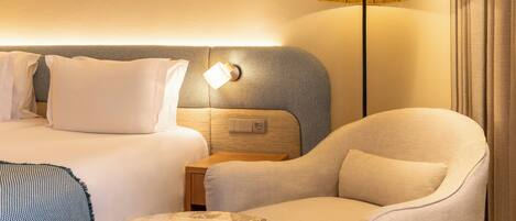 A hotel room with a bed, a nightstand, a lamp, a chair, and a round table.