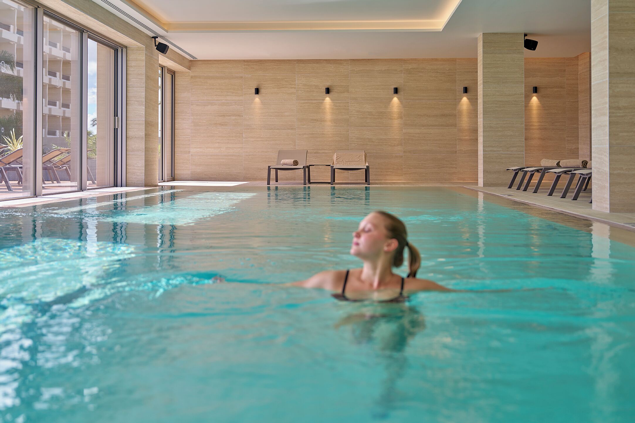 Una piscina interna con acqua cristallina, lettini prendisole e vista sull'esterno.