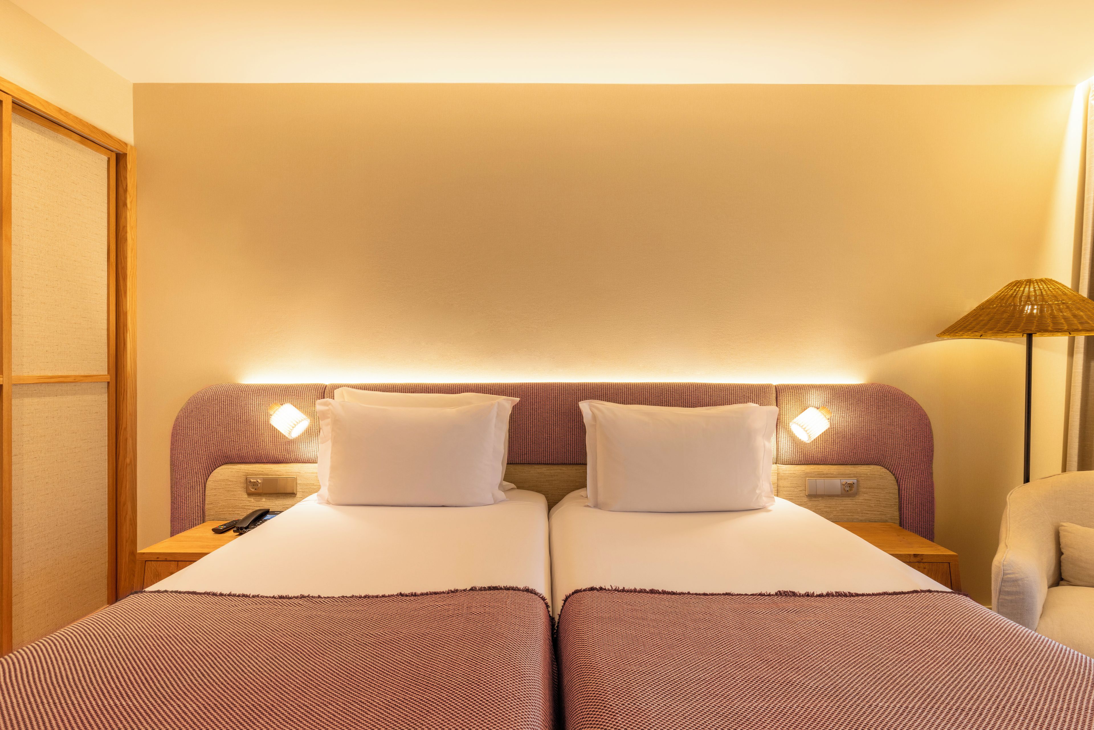 A hotel room with two beds, a nightstand with a lamp, and a chair.