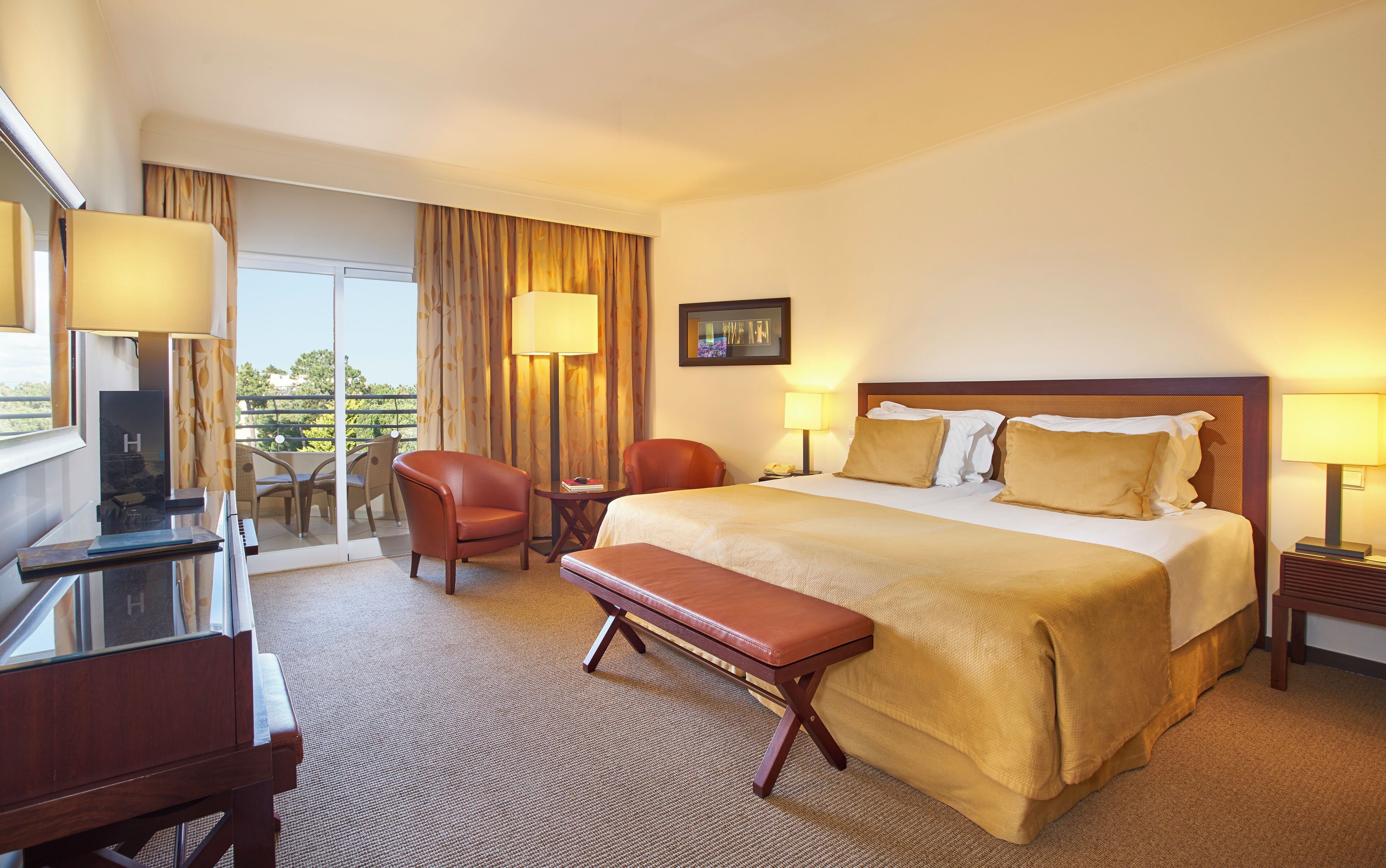 A hotel room with a bed, a desk, a chair, a bench, a TV, and a window with curtains.