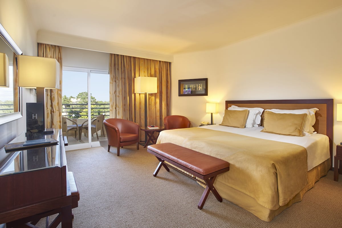 Hotelkamer met een bed, een bureau, een stoel, een bankje, een televisie en een raam met gordijnen.