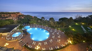 A resort with a large swimming pool surrounded by lounge chairs and a view of the ocean.