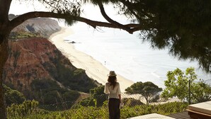A person standing on a balcony overlooking a beach with a cliff in the background.