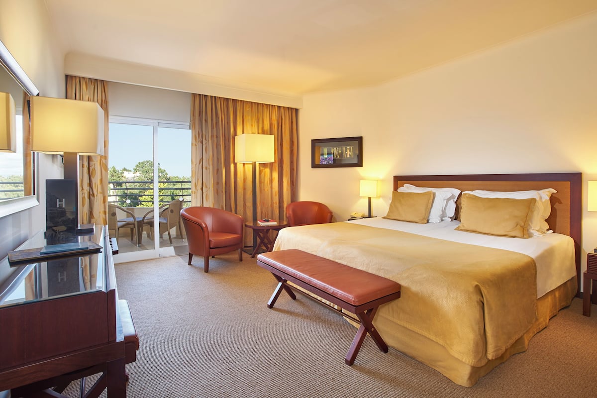 A hotel room with a bed, a desk, a chair, a bench, a TV, and a window with curtains.