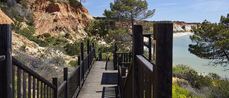 A wooden boardwalk leading to a beach with a rocky cliff and sparse vegetation.