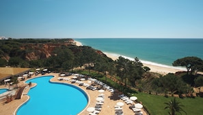 A resort with a swimming pool, beach, and mountainous backdrop.