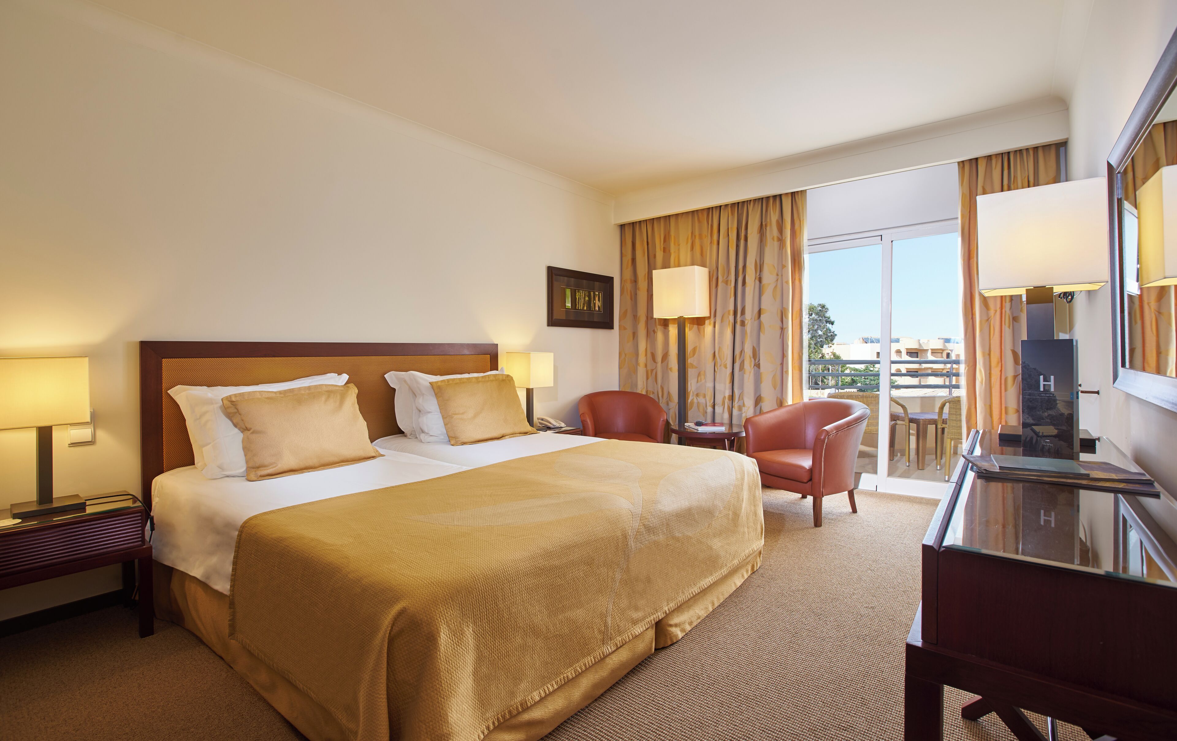 A hotel room with a large bed, a desk, a chair, and a balcony with a view.