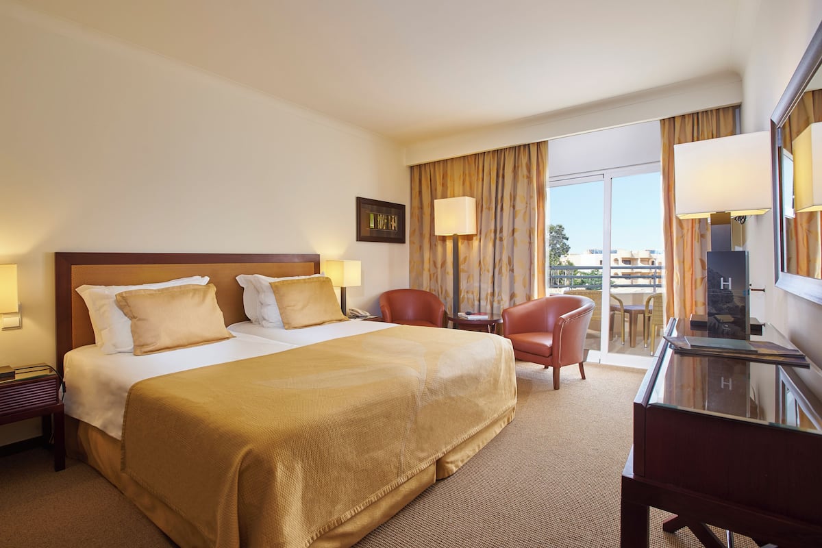 A hotel room with a large bed, a desk, a chair, and a balcony with a view.