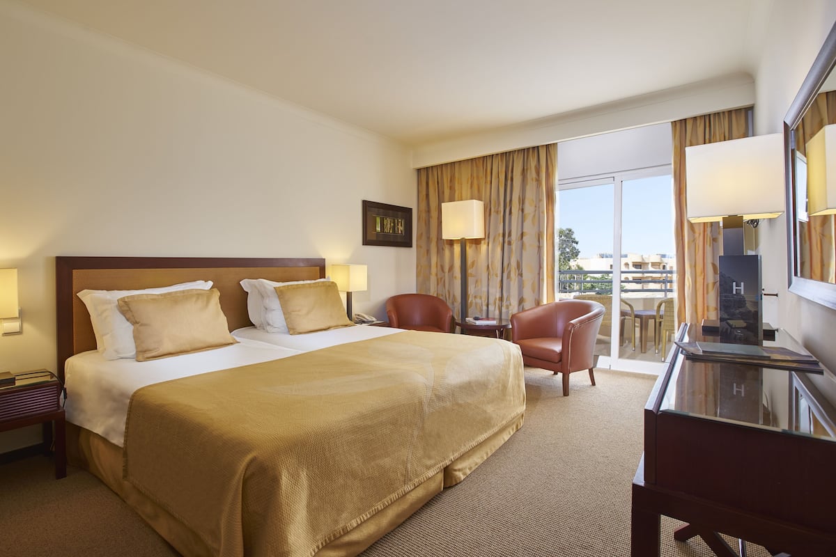 Een hotelkamer met een groot bed, een bureau, een stoel en een balkon met uitzicht.