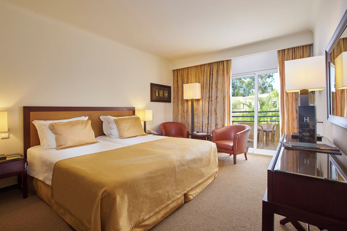 Een hotelkamer met een groot bed, een bureau, een stoel, een televisie en een balkon met gordijnen.