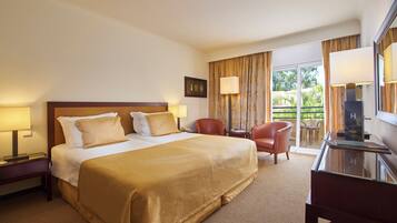 A hotel room with a large bed, a desk, a chair, and a balcony with curtains.