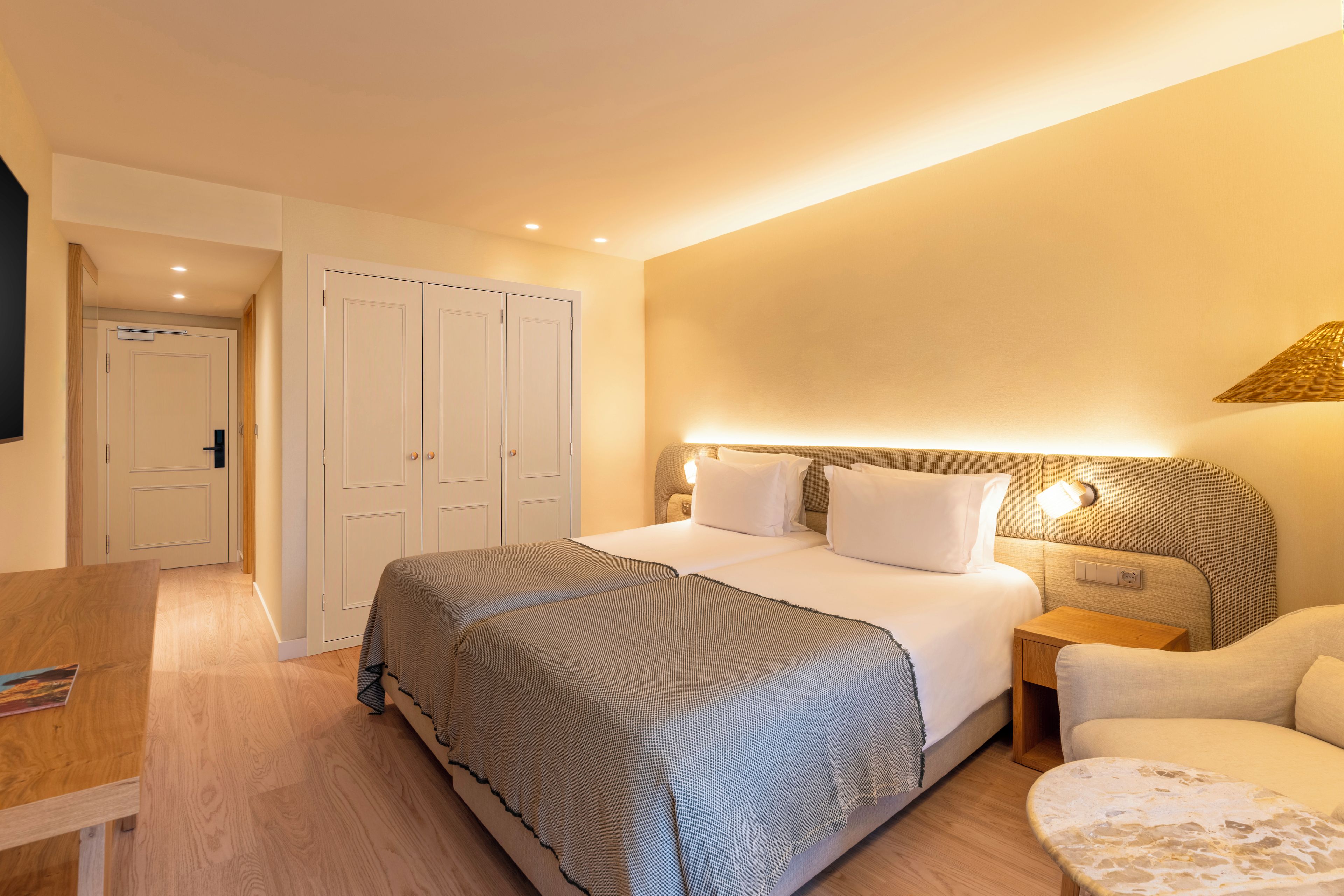 A hotel room with a bed, bedside table, chair, and a desk.