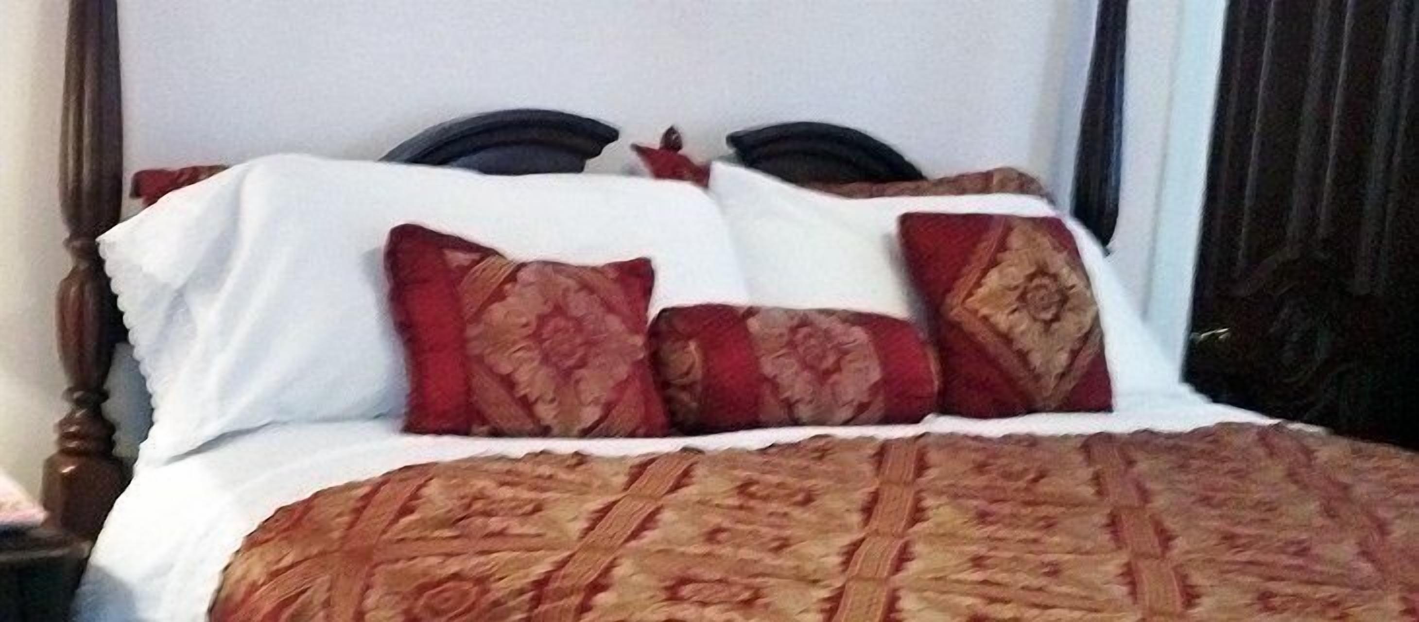 Un lit avec une couvre-lit à motifs et deux oreillers ornés d’un motif rouge et doré.